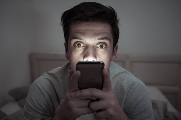 Young mobile phone addict man awake at night in bed using smartphone for chatting, flirting and sending text message. In communication, Internet addiction and Social media network abuse concept - Photo, Image