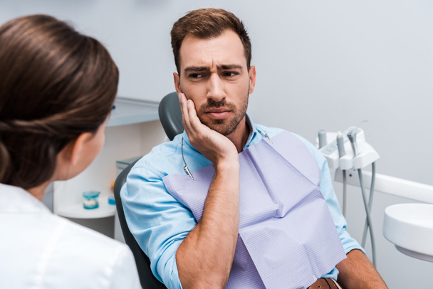 selektywne skupienie rozstroju pacjenta dotykając twarzy podczas gdy ból zębów w pobliżu dentysty  - Zdjęcie, obraz