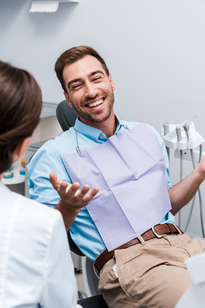 selective focus of cheerful patient gesturing and looking at dentist  - Foto, Imagen