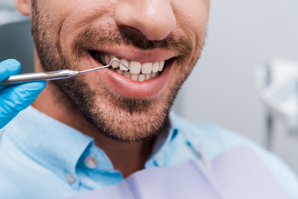 обрезанный вид стоматолога, держащего стоматологический инструмент рядом с веселым человеком
  - Фото, изображение