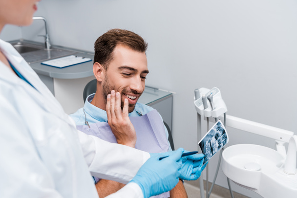 Selektiver Fokus des gut gelaunten Mannes beim Röntgen in Zahnarztnähe im weißen Kittel  - Foto, Bild