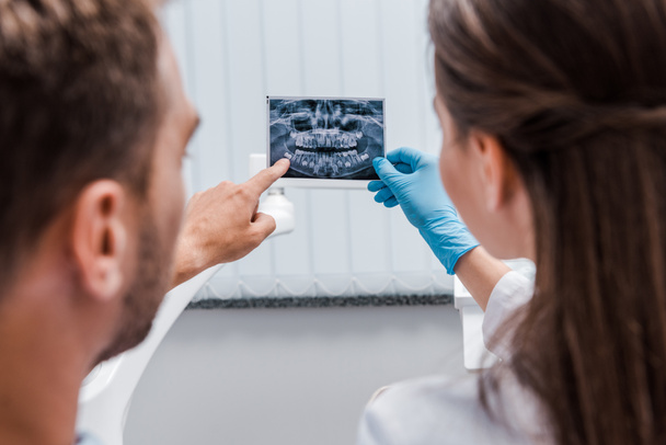 wykadrowany widok dentysta gospodarstwa x-ray w pobliżu pacjenta wskazując palcem w klinice  - Zdjęcie, obraz