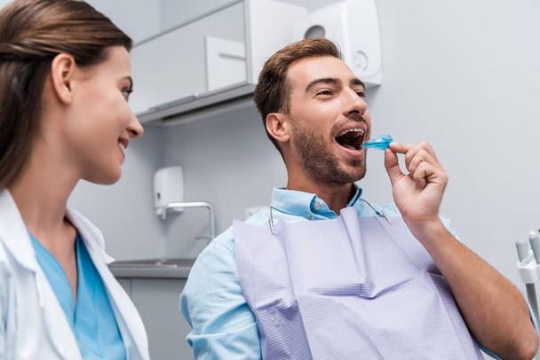 selektywne skupienie pacjenta na wkładaniu uchwytu w usta w pobliżu szczęśliwego dentysty  - Zdjęcie, obraz