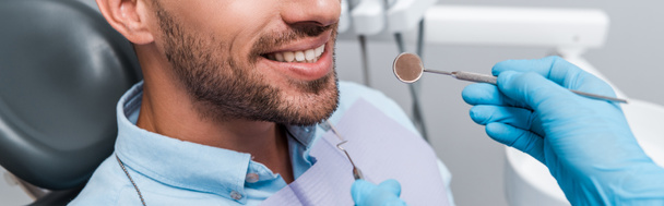 Panoramaaufnahme eines Zahnarztes in Latexhandschuhen, der zahnärztliche Instrumente in der Nähe des Patienten hält  - Foto, Bild