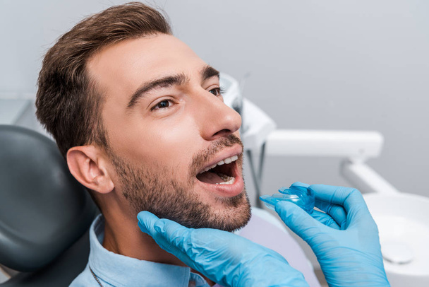 cropped view of dentist in blue latex gloves holding retainer near bearded man  - 写真・画像