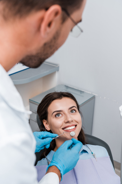επιλεκτική εστίαση του ανθρώπου σε γάντια λατέξ που κατέχουν οδοντιατρικά όργανα κοντά σε ελκυστική γυναίκα  - Φωτογραφία, εικόνα