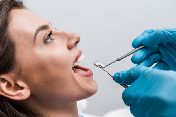 bijgesneden weergave van tandarts in latex handschoenen houden tandheelkundige instrumenten in de buurt van aantrekkelijke vrouw  - Foto, afbeelding