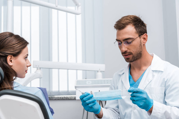 selective focus of handsome man in glasses holding medical mask near attractive patient  - Photo, Image