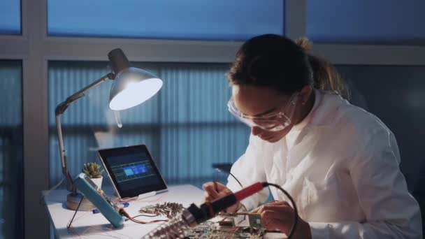 Primo piano centrale di ingegnere donna di elettronica in cappotto bianco e occhiali protettivi controllando scheda madre con tester multimetro
 - Filmati, video
