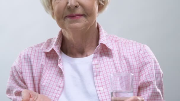 Smiling elderly woman showing pills and glass of water at camera, health care - Imágenes, Vídeo
