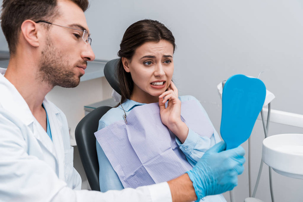 selective focus of girl looking in mirror and touching face near handsome dentist  - Photo, Image