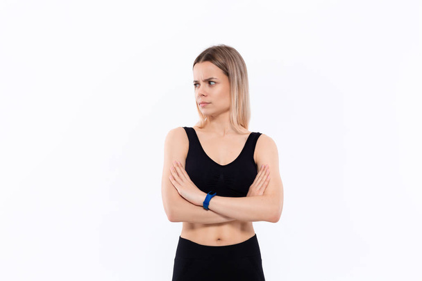 Young sporty blond woman in a black sportswear with smart watches for pulse measuring keeping hands crossed standing over white background. - Photo, Image