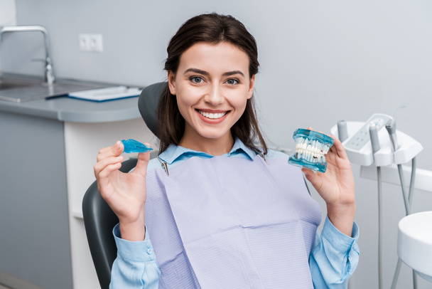 cheerful young woman holding teeth model and retainer in hands  - Photo, Image