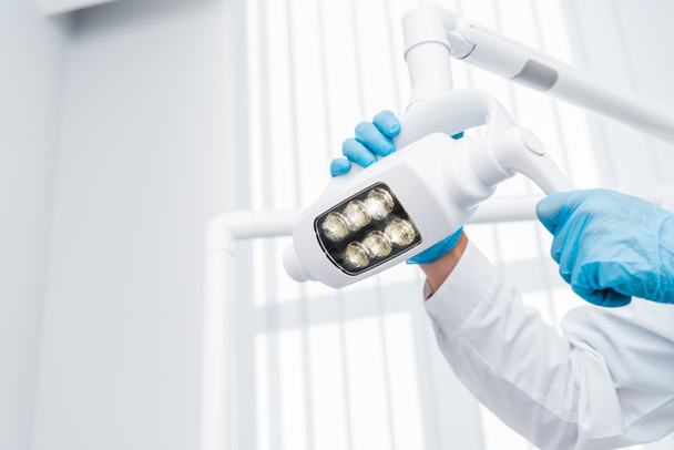 cropped view of dentist in latex gloves touching medical lamp  - Photo, Image