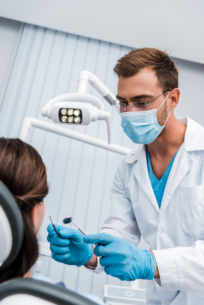селективная направленность стоматолога в очках и медицинской маске, держащей стоматологические инструменты рядом с женщиной
  - Фото, изображение