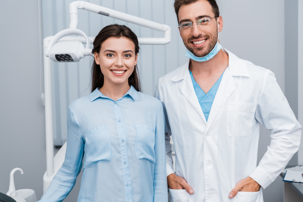 cheerful girl smiling near handsome dentist standing with hands in pockets  - Photo, Image