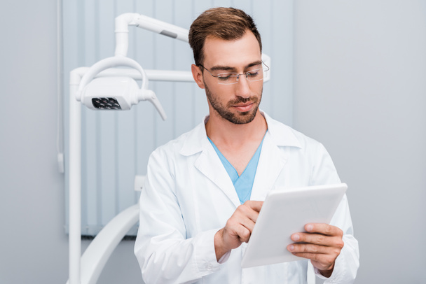 homem bonito em casaco branco e óculos usando tablet digital na clínica
  - Foto, Imagem