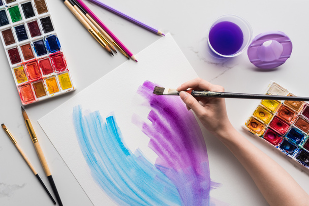 vista recortada de artista dibujo púrpura y azul acuarela pinceladas sobre papel blanco sobre mármol superficie blanca
 - Foto, imagen