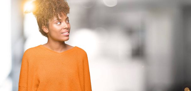 Mooie jonge Afro-Amerikaanse vrouw op geïsoleerde achtergrond op zoek weg aan kant met glimlach op het gezicht, natuurlijke wijze van uitdrukking. Lachen vertrouwen. - Foto, afbeelding