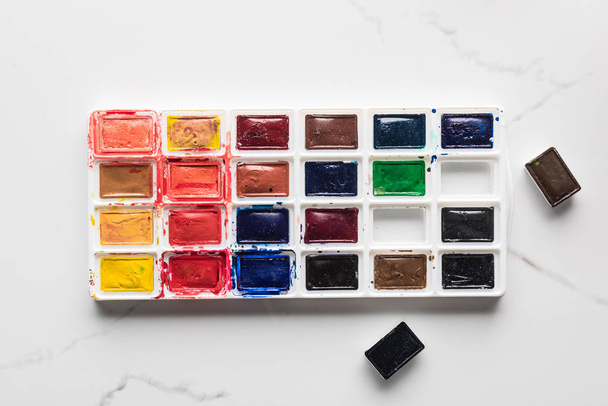 watercolor bright paint palette with missing pieces on marble white surface - Photo, Image