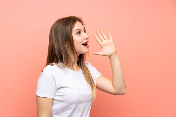 Tiener meisje over geïsoleerde roze muur schreeuwen met mond wijd open - Foto, afbeelding