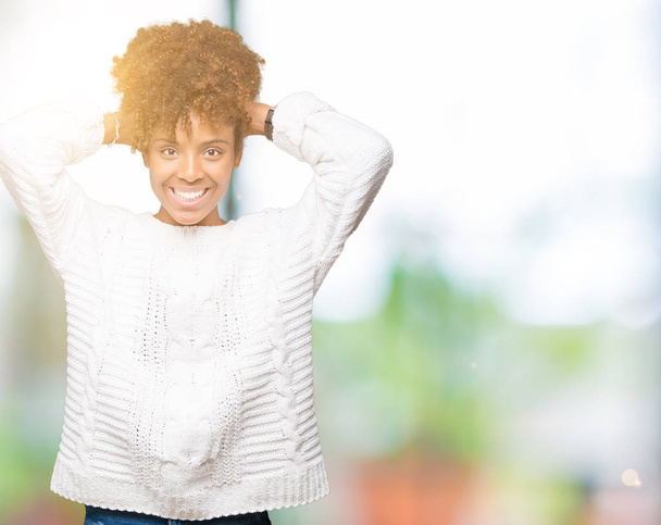 Linda jovem afro-americana vestindo camisola de inverno sobre fundo isolado Relaxando e esticando com braços e mãos atrás da cabeça e pescoço, sorrindo feliz
 - Foto, Imagem