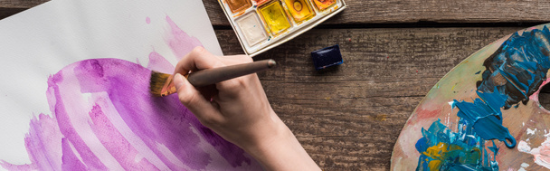 bijgesneden beeld van de kunstenaar tekening in schetsboek met aquarel verven op houten tafel, panoramische schot - Foto, afbeelding