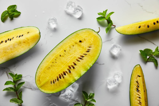 top view of cut delicious exotic yellow watermelon with seeds on marble surface with mint, ice - Foto, Imagem