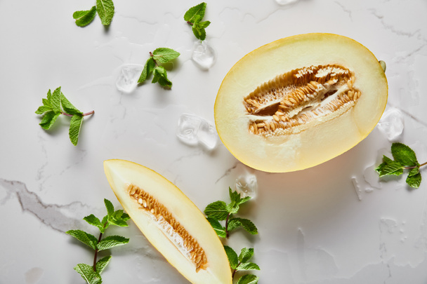 Draufsicht auf geschnittene köstliche Melone mit Samen auf Marmoroberfläche mit Minze und Eis - Foto, Bild
