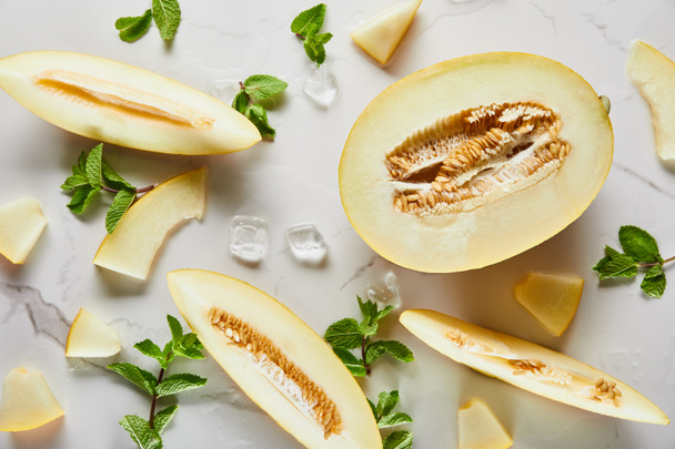 Blick von oben auf geschnittene köstliche Melone auf Marmoroberfläche mit Minze und Eis - Foto, Bild