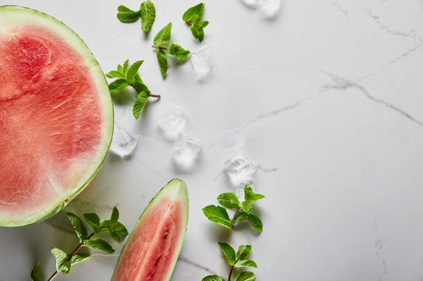 Draufsicht auf geschnittene köstliche rote Wassermelone auf Marmoroberfläche mit Minze und Eis - Foto, Bild