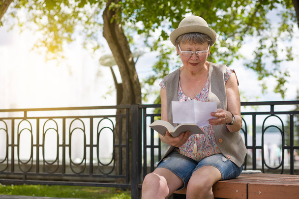 Egy idős nő olvasott levelet vagy dokumentumot ül a padon, a nyári. - Fotó, kép