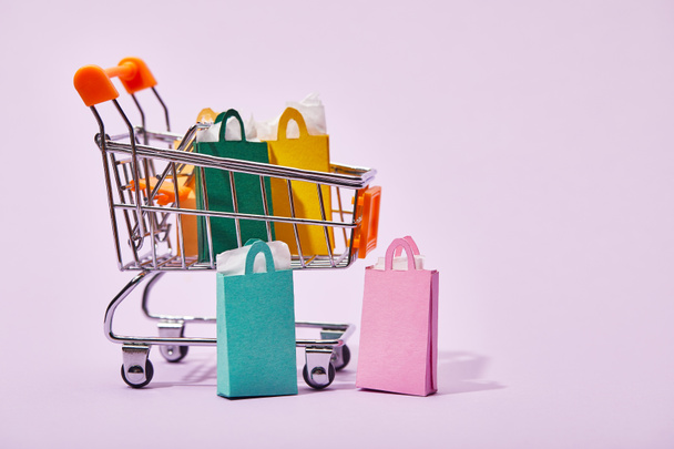  carro de juguete con bolsas de papel de colores cerca de algunas bolsas de compras sobre fondo violeta
 - Foto, Imagen
