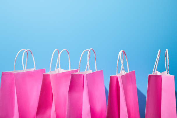 alguns sacos de compras de papel rosa com alças brancas no fundo azul
  - Foto, Imagem