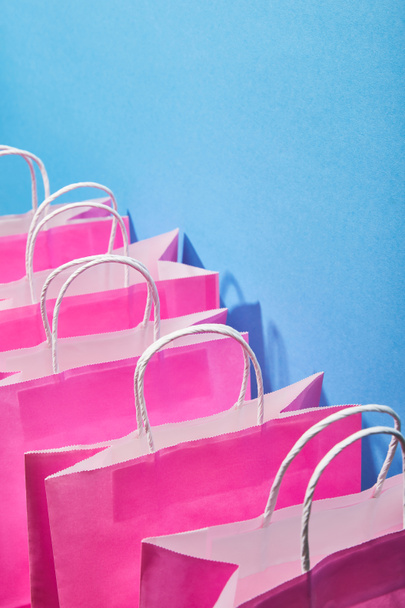 pink shopping bags with white handles on blue background  - Fotoğraf, Görsel