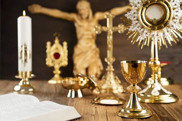 The Cross, monstrance, golden chalice and Bible on the wooden altar. - Photo, Image