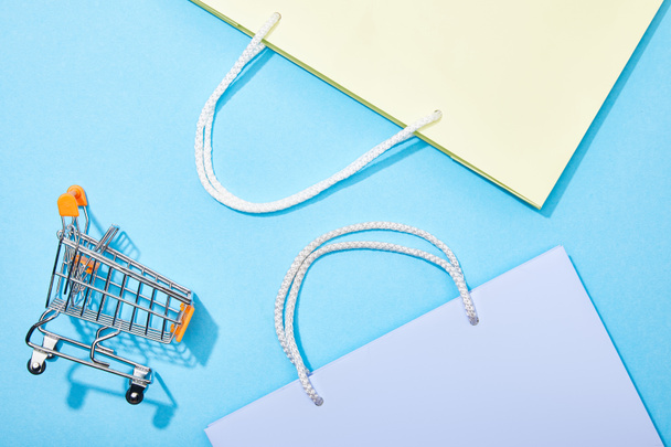 top view of shopping bags near toy shopping cart on blue  - Foto, Imagen