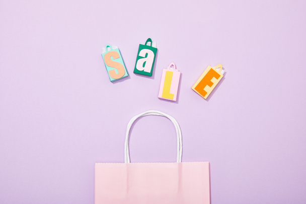 κορυφή θέα των πολύχρωμων σακούλες παιχνιδιών με πώληση επιγραφή κοντά σε ροζ τσάντα για ψώνια σε βιολετί - Φωτογραφία, εικόνα