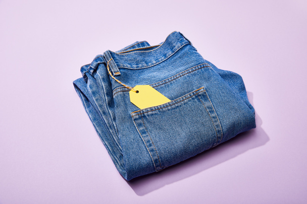 jeans with yellow paper sale tag on rope on violet background - Foto, Imagem