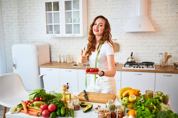 Jeune femme heureuse tenant des tomates pour faire de la salade dans la belle cuisine avec des ingrédients frais verts à l'intérieur. Aliments sains et régime concept. Perdre du poids
 - Photo, image