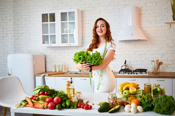 Joven mujer feliz sosteniendo hojas de lechuga para hacer ensalada en la hermosa cocina con ingredientes frescos verdes en el interior. Comida saludable y concepto de dieta. Perder peso
 - Foto, Imagen
