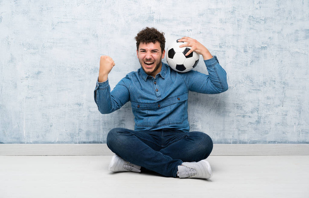 Joven sentado en el suelo sosteniendo una pelota de fútbol
 - Foto, imagen
