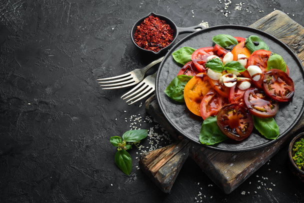 Caprese salad on a black plate. Tomatoes, mozzarella cheese and basil. Top view. Free space for your text. - Zdjęcie, obraz