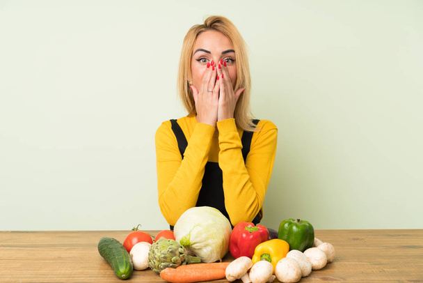 Mujer rubia joven con un montón de verduras con expresión facial sorpresa
 - Foto, imagen