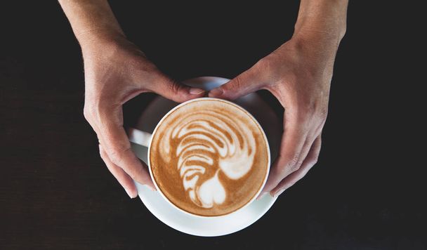 Una taza de café con leche sobre fondo negro. Foto hecha en clave oscura
. - Foto, Imagen