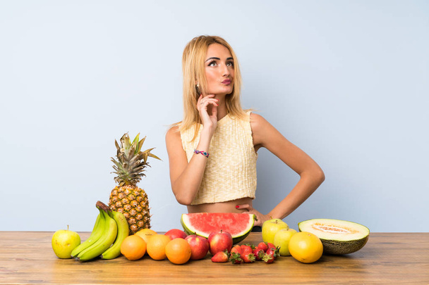 Nuori blondi nainen, jolla on paljon hedelmiä ajattelu idea
 - Valokuva, kuva