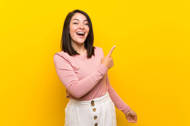Young Mexican woman over isolated yellow background surprised and pointing side - Photo, Image