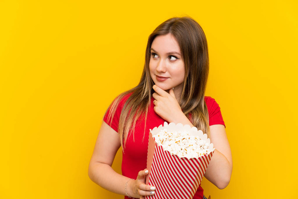 Nuori nainen popcorneja vaaleanpunainen seinä ajattelu idea
 - Valokuva, kuva