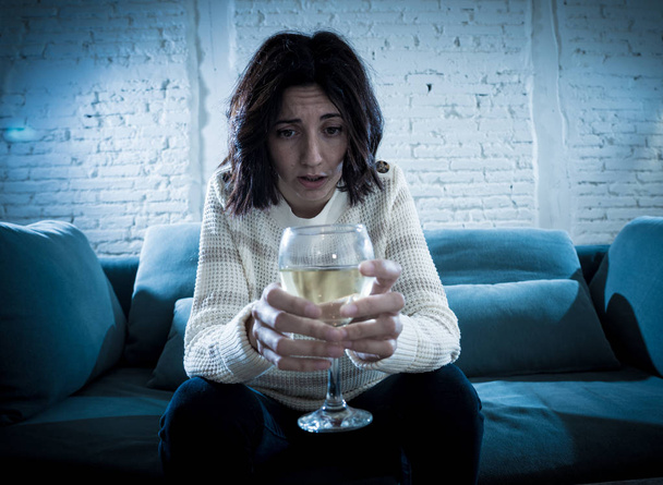 Stressed and hopeless young woman drinking a glass of wine alone at home. Feeling depressed, frustrated and weak, trying to feel better drinking. Unhealthy behavior, depression and alcoholism concept. - Fotó, kép