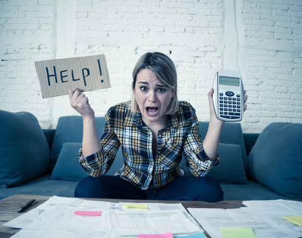 Worried young woman feeling stressed while accounting business and home finances. Desperate showing Help sign and calculator. In bad economic situation, paying debts, bills and financial problems. - Photo, Image